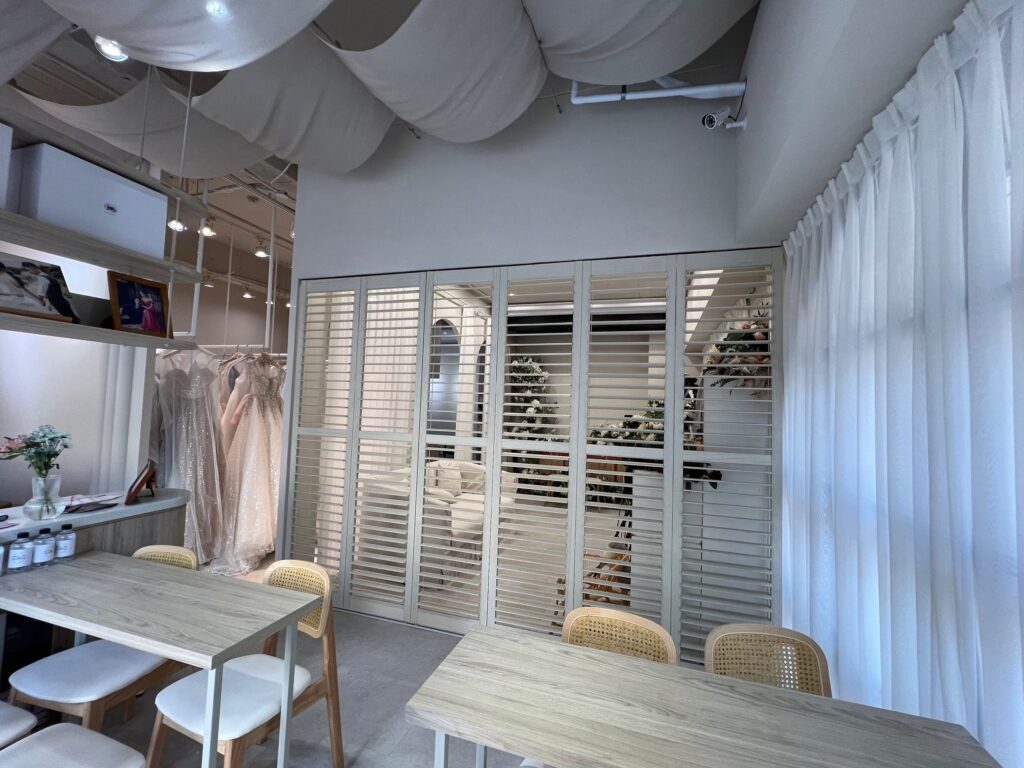 婚紗禮服店採用百葉窗門來作為隔間，不僅方便讓空間通透，也能提供穿戴衣服時的臨時性隱密空間需求。尤其質感比其他隔間更搭配，白灰木百葉與白色禮服簡直就是天作之合。